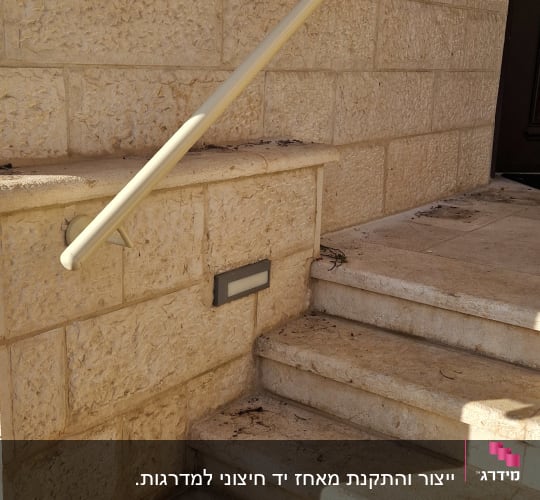 מאחז יד ממתכת מותקן על קיר אבן לצד מדרגות כניסה